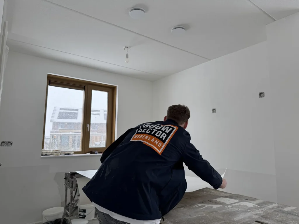 Behanger van Bouwsector Nederland in werkjas pakt een baan van de plaktafel in een nieuwbouwwoning