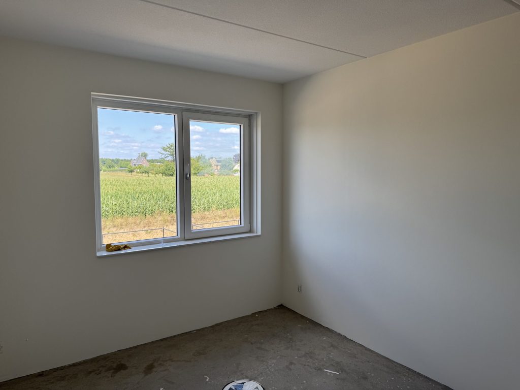 Lege nieuwbouwkamer met gladde lichte wanden en een raam, klaar voor de wandafwerking
