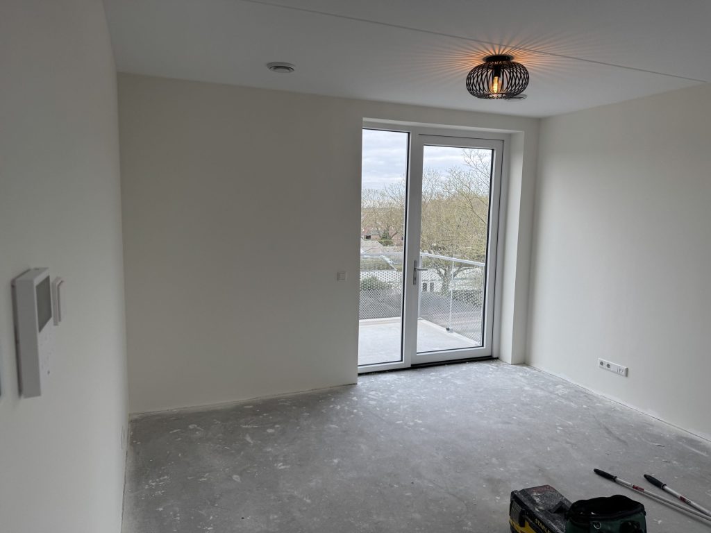 Lege kamer in een nieuw appartement met openslaande deuren naar het balkon, kort na de oplevering